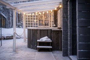 Una sauna d'exterior de fusta amb una banca, una porta de vidre amb detalls en forma de cor i llums penjades.