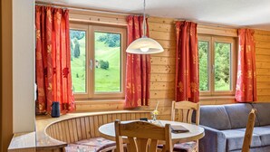 Un intérieur en bois avec une table ronde, des chaises, un canapé et une fenêtre avec des rideaux.