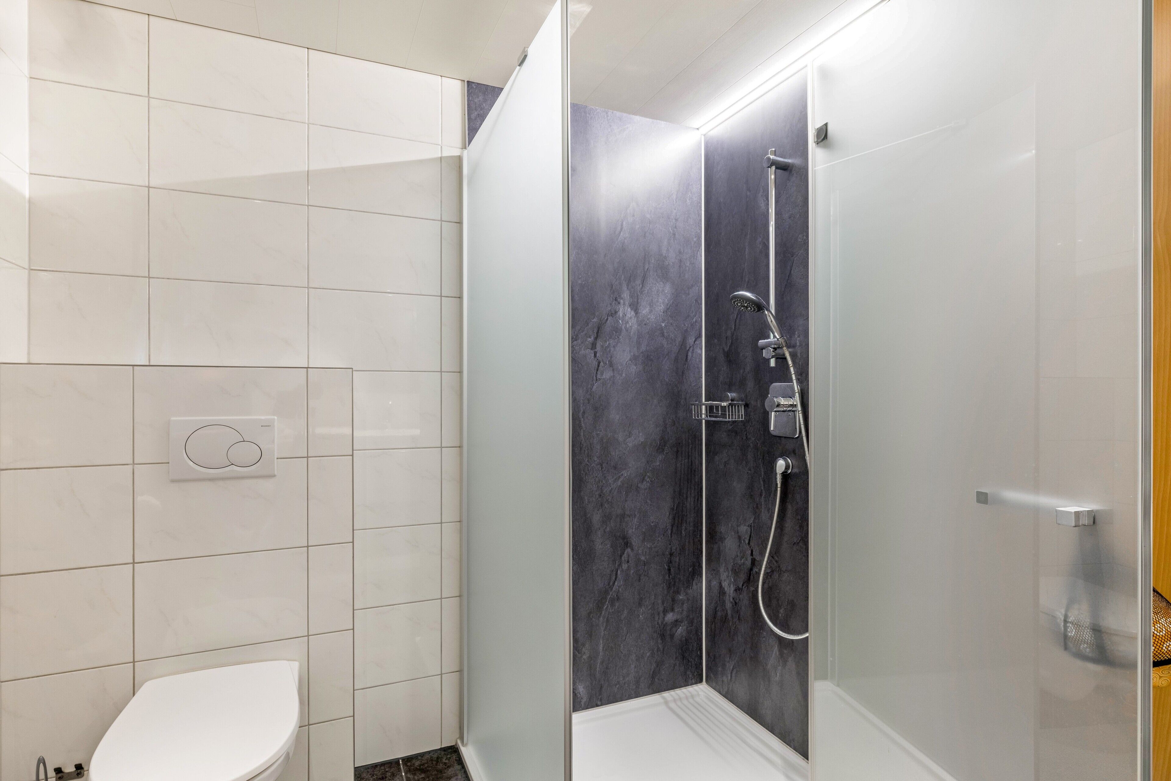 Un baño con inodoro, ducha con puerta de cristal y panel de control en la pared.