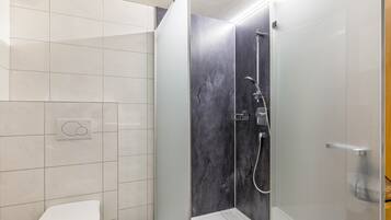 Un baño con inodoro, ducha con puerta de cristal y panel de control en la pared.