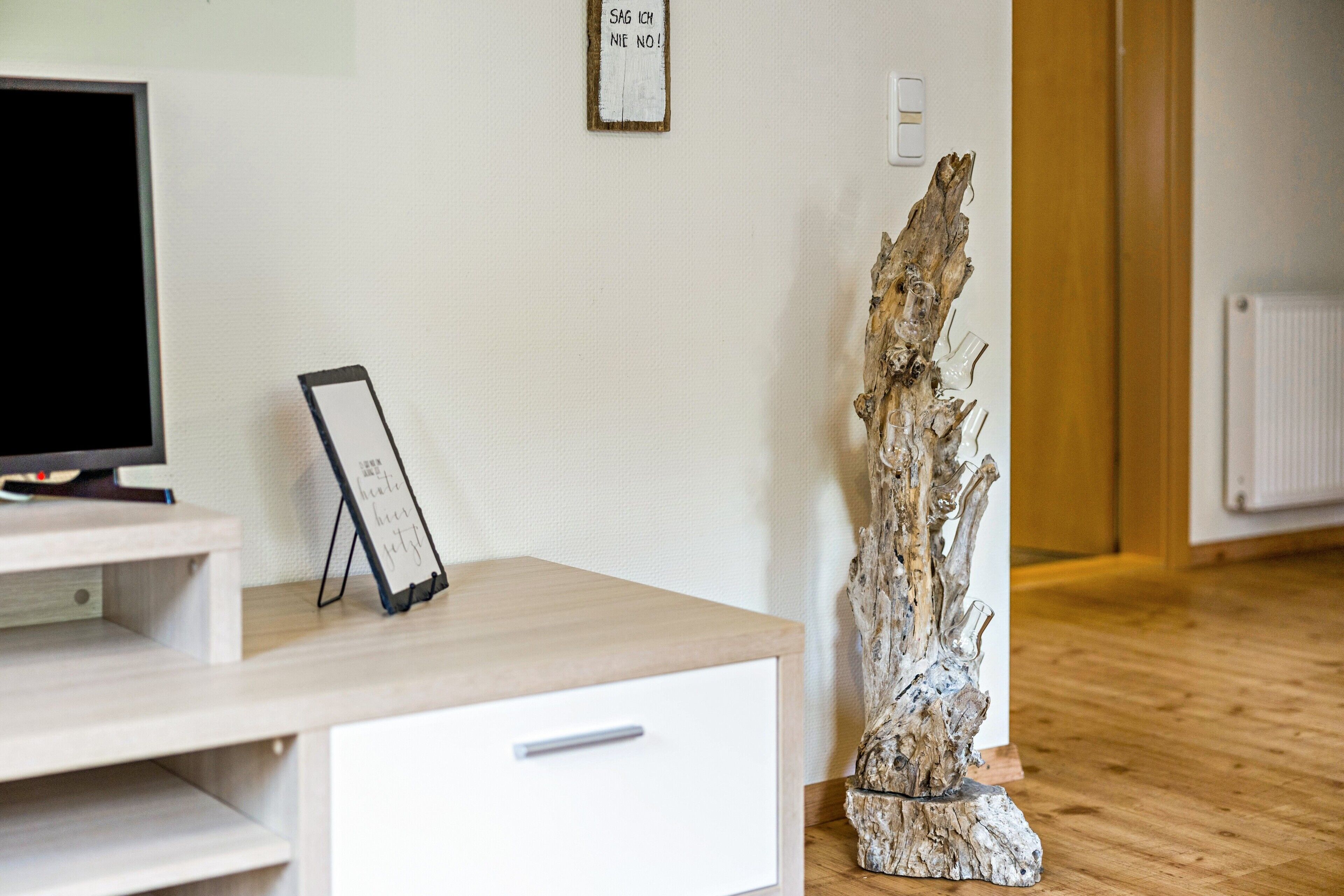 Une pièce comprenant un bureau en bois, un téléviseur, un tronc d’arbre décoratif et un panneau fixé au mur.