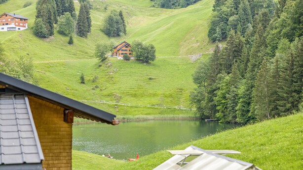 Une maison avec un toit en pente, un étang et une colline boisée.
