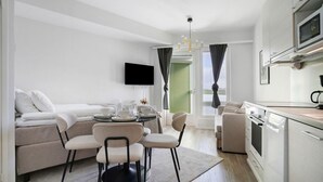 Ein modernes Wohnzimmer mit einer Couch, Sesseln, einem Esstisch und einer Küchenzeile mit Geräten.
