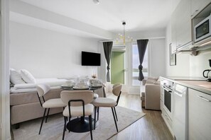 Ein modernes Wohnzimmer mit einer Couch, Sesseln, einem Esstisch und einer Küchenzeile mit Geräten.