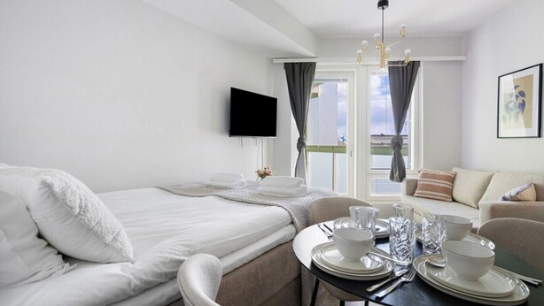 Ein Hotelzimmer mit einem Bett, einem Esstisch für zwei Personen, einer Couch, einem an der Wand montierten Fernseher und Blick ins Freie.
