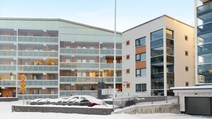 Ein mehrstöckiges Gebäude mit Glasfassade, ein Parkplatz mit schneebedeckten Autos und ein klarer Himmel.