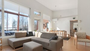 Een moderne woonkamer met een modulaire bank, een voetenbankje, en een eethoek met houten stoelen en een tafel.