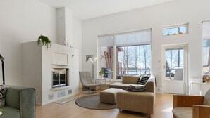 Een ruime woonkamer met een open haard, een groot raam en uitzicht op de omgeving.