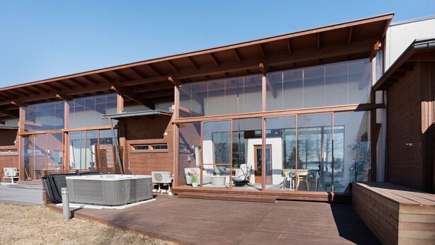 Een modern gebouw met grote glasramen, een houten terras en tuinmeubilair.