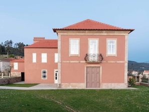 Un edificio de dos pisos con techo de tejas rojas, un balcón central con ornamentación metálica y una puerta con un ventanal arriba.