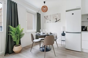 Ein kompakter Wohnbereich mit Essplatz, einem Blumentopf, einer modernen Lampe und einem weißen Kühlschrank.