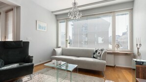 A modern living room with a grey sofa, a black armchair, a glass coffee table, and a chandelier. - Aurora City Apartment 3bdr By Lapland Host (Rovaniemi)
