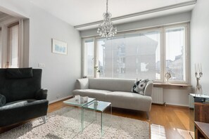 Ein modernes Wohnzimmer mit einem grauen Sofa, einem schwarzen Sessel, einem Glastisch und einer Deckenleuchte.