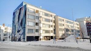 A multi-story building with a large mural on the side, multiple windows, and a snow-covered ground. - Aurora City Apartment 3bdr By Lapland Host (Rovaniemi)