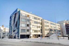 Ein mehrstöckiges Gebäude mit einer großen Wandmalerei an der Seite, zahlreichen Fenstern und einem verschneiten Untergrund.