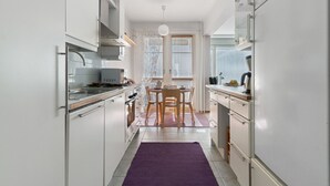 A modern kitchen with white cabinets, a dining area with a table and chairs, and a purple rug. - Aurora City Apartment 3bdr By Lapland Host (Rovaniemi)