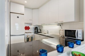 A modern kitchen with white cabinets, a stove, a coffee maker, a microwave, and blue glass cups on the counter. - City Center Apartment Free Parking By Lapland Host (Rovaniemi)