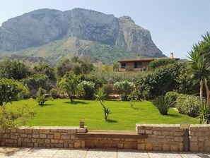 Ein Haus mit einer Steinwand im Vordergrund, einem gepflegten Rasen und einem Berg im Hintergrund.