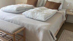 Un dormitorio con cama, almohadas, mesitas de noche, una lámpara y un banco de madera.