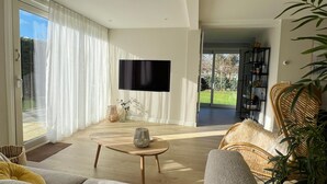 Una sala de estar moderna con una televisión de pantalla plana, un sofá, una mesa de centro y una silla de mimbre.