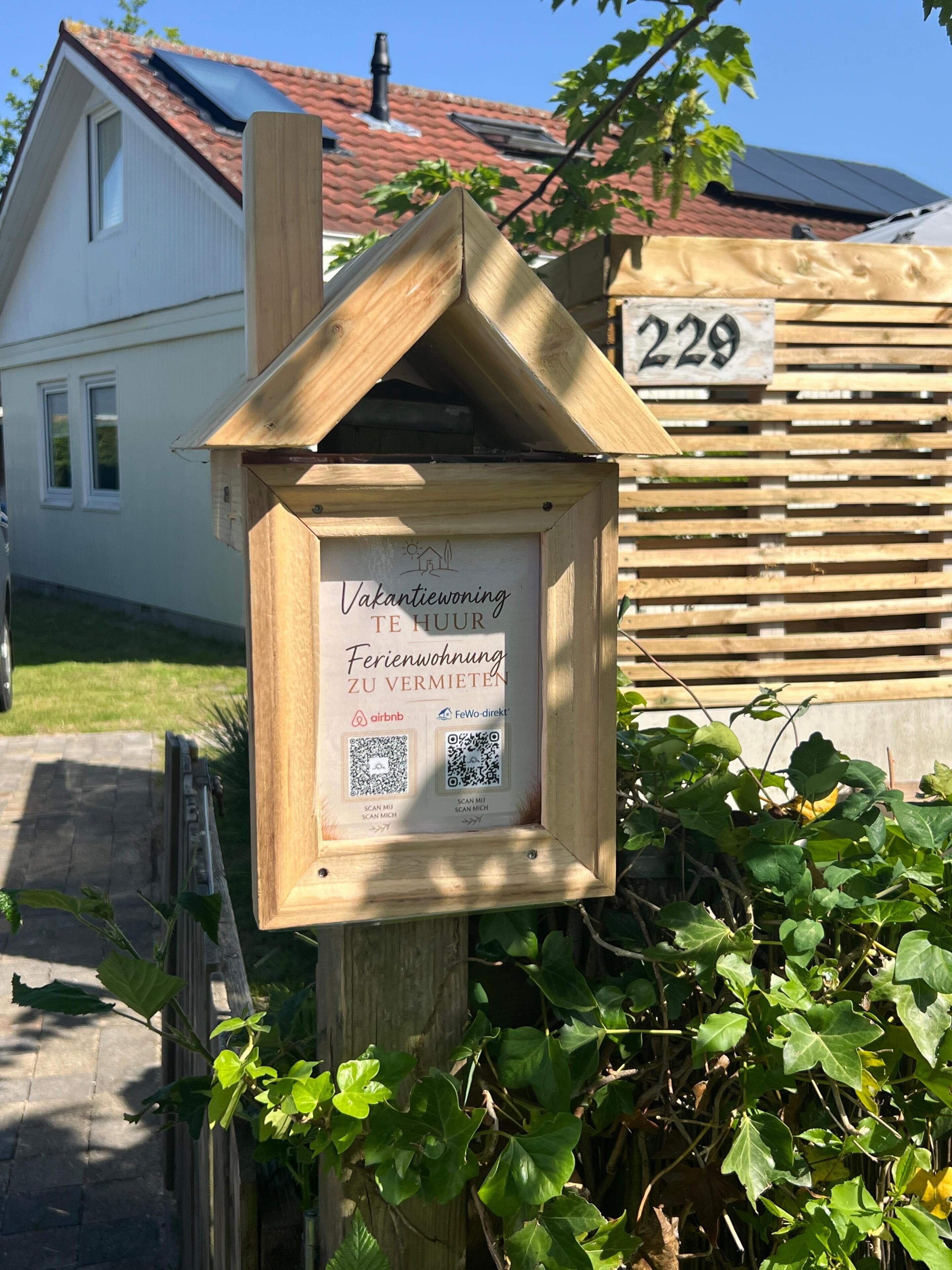 A wooden sign with QR codes and text for booking a vacation home.
