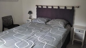 Quarto com cama, mesa de cabeceira, uma cadeira e uma obra de arte na parede.