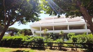 Um edifício de vários andares com telhado plano, rodeado por vegetação e árvores.