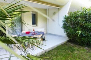 A patio area with a table and chairs, a window, and a hedge. - Superb T2 apartment in secure luxury residence with swimming pool and garden. (La Grande-Motte)