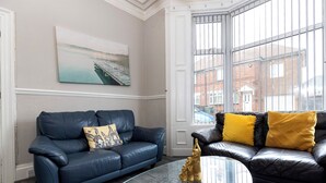 Ein Wohnzimmer mit einem blauen Ledersofa, einem Glastisch und einem Bild an der Wand.