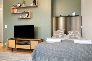 Una camera da letto moderna con televisione a schermo piatto, mensole in legno, un letto con cuscini decorati e un comodino con telecomando.