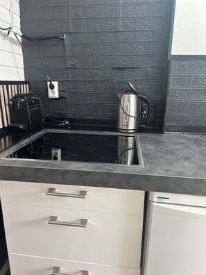 A kitchen with a black backsplash, stainless steel appliances, and white cabinetry. - Cozy summer cottage 200 meters from the beach! (Noordwijk)
