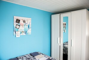 A room with a blue wall, a bed with a patterned bedspread, a white wardrobe, and a wall decoration with motivational phrases. - Cozy summer cottage 200 meters from the beach! (Noordwijk)