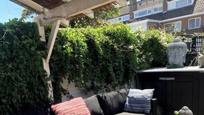 Une terrasse extérieure avec un canapé, des coussins, une table et une statue de Bouddha.
