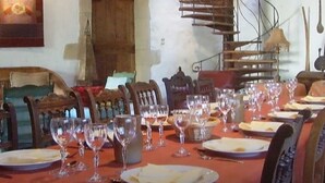 Un comedor con una mesa larga dispuesta para una comida, sillas y una escalera de caracol al fondo.