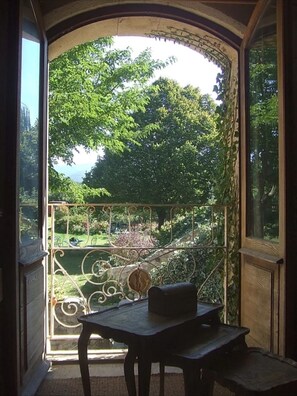 Ein Zimmer mit Blick auf einen Garten durch eine geöffnete Tür, ein Tisch mit einem Stuhl und ein schmiedeeisernes Geländer.