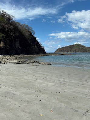 Ein Strand mit felsigem Ufer, ruhigem Wasser und einer entfernten Hügelkette.