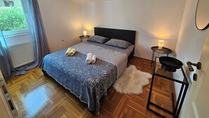 Une chambre à coucher avec un lit, deux lampes de chevet, un radiateur, un plancher en bois et une vue par la fenêtre.