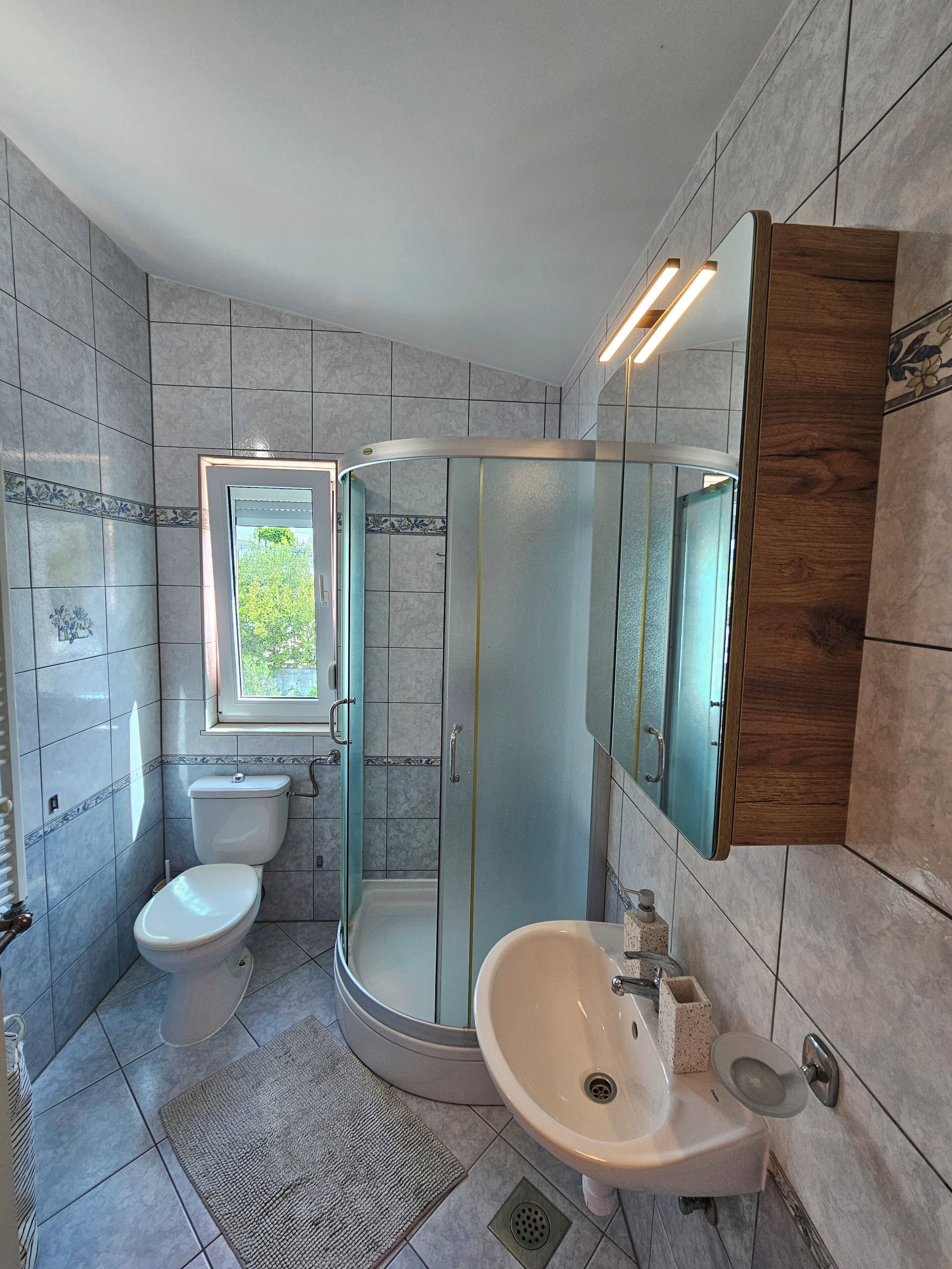 Une salle de bain moderne équipée de toilettes, d’un lavabo, d’une douche et d’une fenêtre.