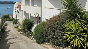 Un bâtiment situé sur la côte, doté d’un balcon, avec un ciel dégagé et un bateau en arrière-plan.