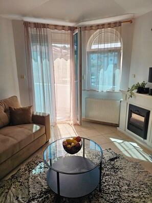 A living room with a sofa, a glass coffee table with fruit, a fireplace, and a view through a window. - Luna Mare, One-Bedroom Apartment on Čiovo (Trogir)