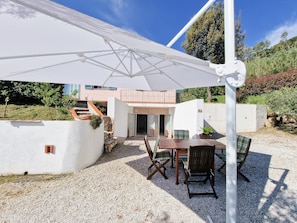 Un patio con una mesa, sillas, un paraguas blanco y un edificio con balcón.