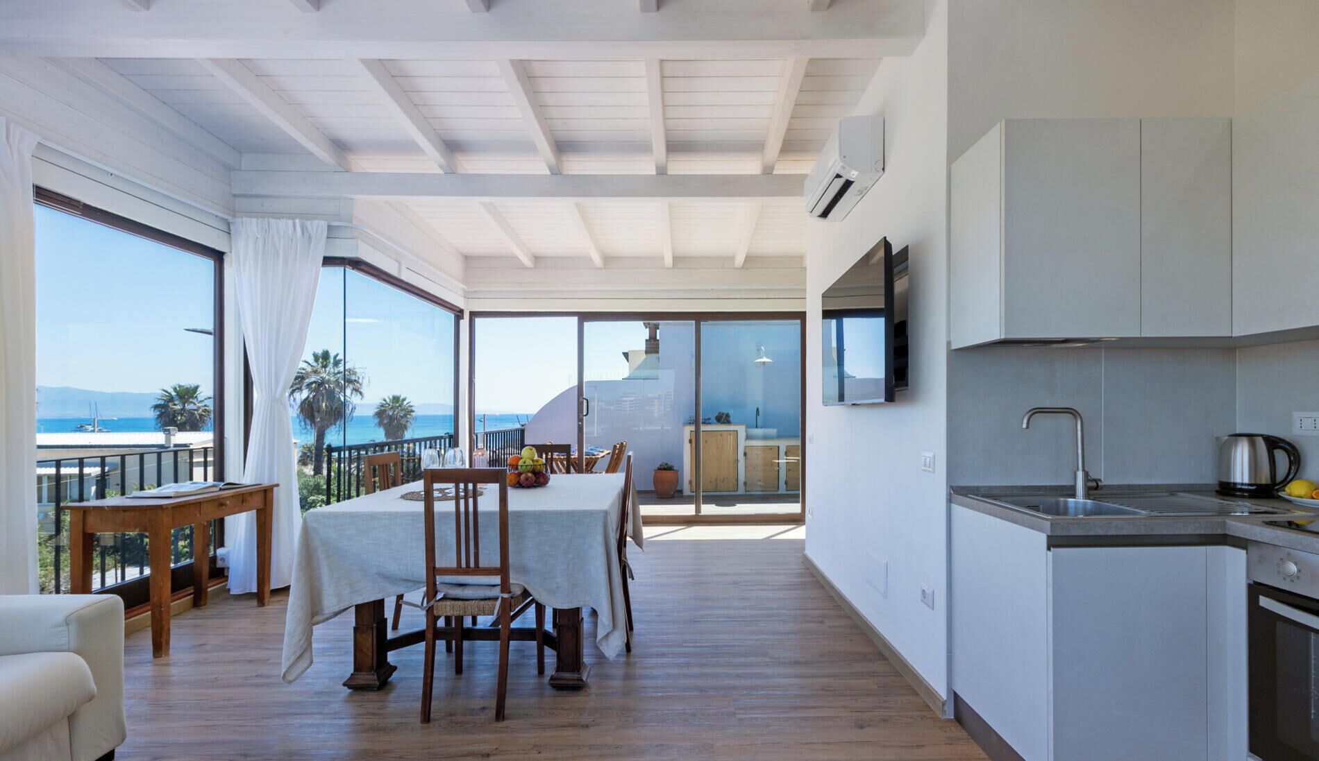 Una cucina moderna con vista sul mare, un'area pranzo con tavolo e sedie, e un balcone con ringhiera.
