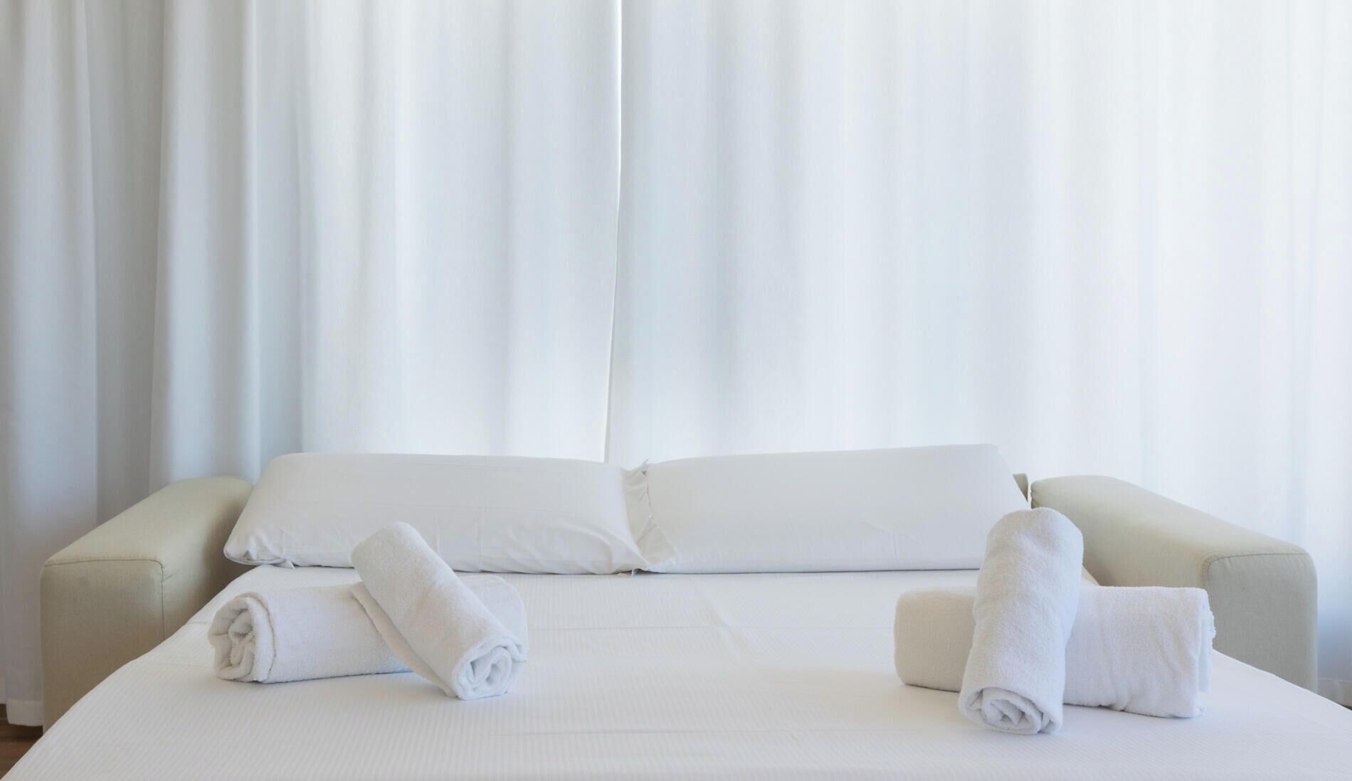 Une chambre d’hôtel avec un lit, deux oreillers et deux serviettes enroulées.