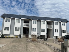 Un immeuble d’appartements à plusieurs étages, à l’extérieur gris, doté de nombreux balcons et d’une allée en béton.