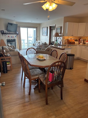 Un coin repas avec une table et des chaises en bois, une cuisine avec des meubles blancs et un ventilateur de plafond.