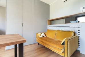 A modern room with a wooden table, a sofa with a cushion, and a built-in bench with storage. - Bright 41m2 studio apartment, ideal for 2 people, located on the third floor of a building with lift.The accommodation is located in a quiet residential area, known for its direct view of the Parco Nord Milano.Served by the Milano Bruzzano FN station (su (Milano)
