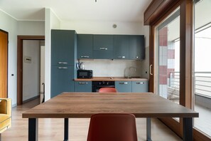 A modern kitchen with teal cabinets, a wooden dining table, and a red chair. - Bright 41m2 studio apartment, ideal for 2 people, located on the third floor of a building with lift.The accommodation is located in a quiet residential area, known for its direct view of the Parco Nord Milano.Served by the Milano Bruzzano FN station (su (Milano)