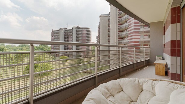 Ein Balkon mit Blick auf hohe Gebäude, einer Drahtgitter-Absturzsicherung und einer gepolsterten Sitzecke.