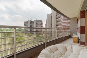 Ein Balkon mit Blick auf hohe Gebäude, einer Drahtgitter-Absturzsicherung und einer gepolsterten Sitzecke.