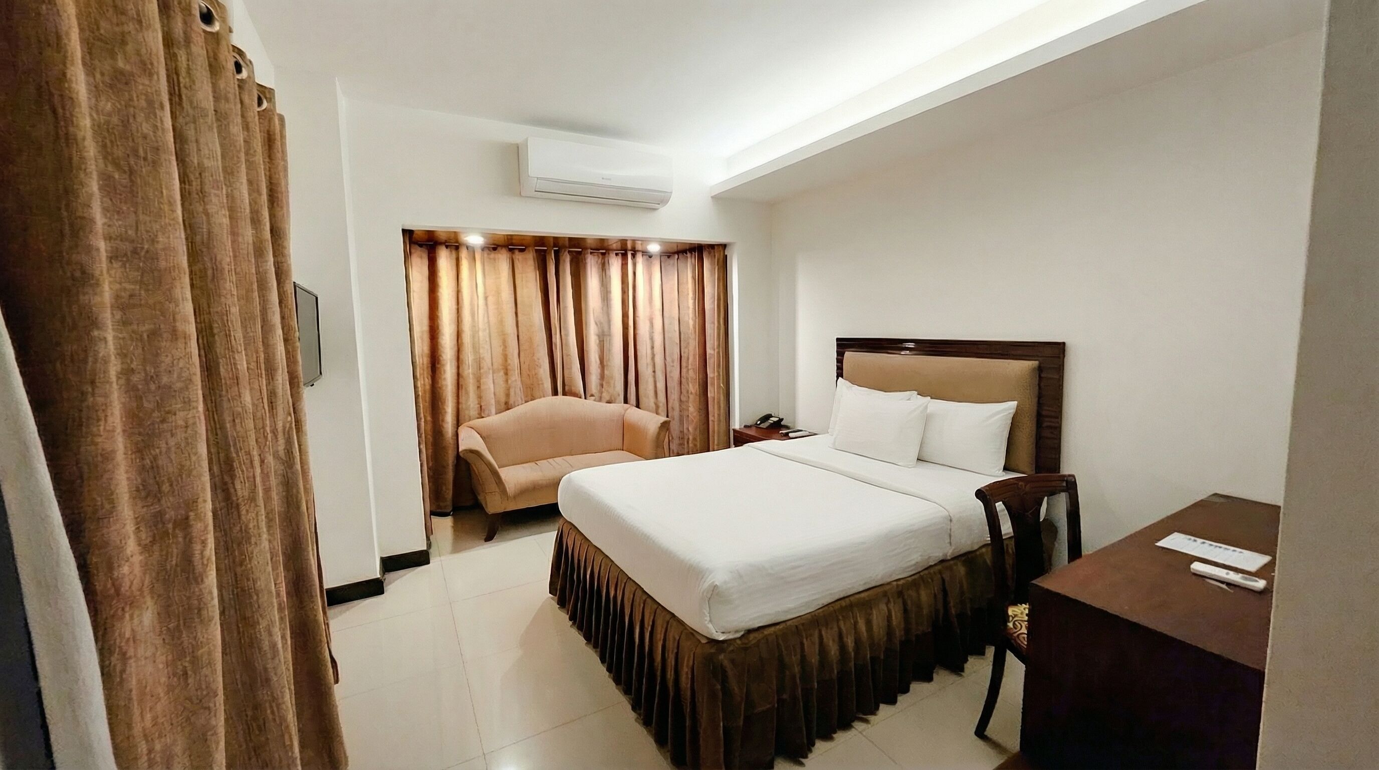Ein Hotelzimmer mit Bett, Stuhl, Schreibtisch und Vorhang.